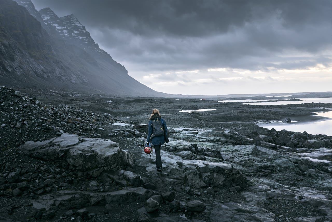 Hiker with a backpack traversing a rocky Icelandic landscape under a dramatic cloudy sky.